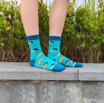 Person wearing blue socks with swimming kids on a stone ledge with greenery in the background