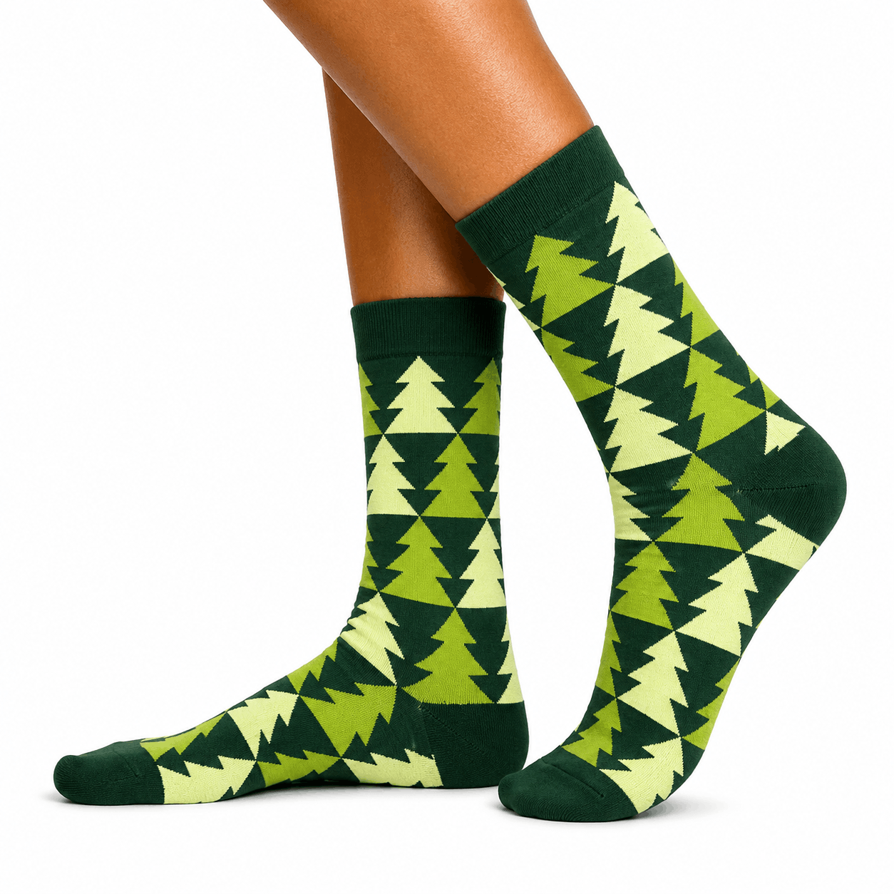 A pair of crew socks with a green and light green Christmas tree pattern, shown on a person's feet against a white background.