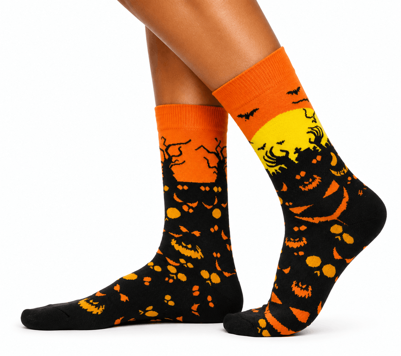A pair of crew socks worn on a person's feet, featuring a Halloween design with orange and black jack-o'-lantern patterns and a yellow full moon on a black background.