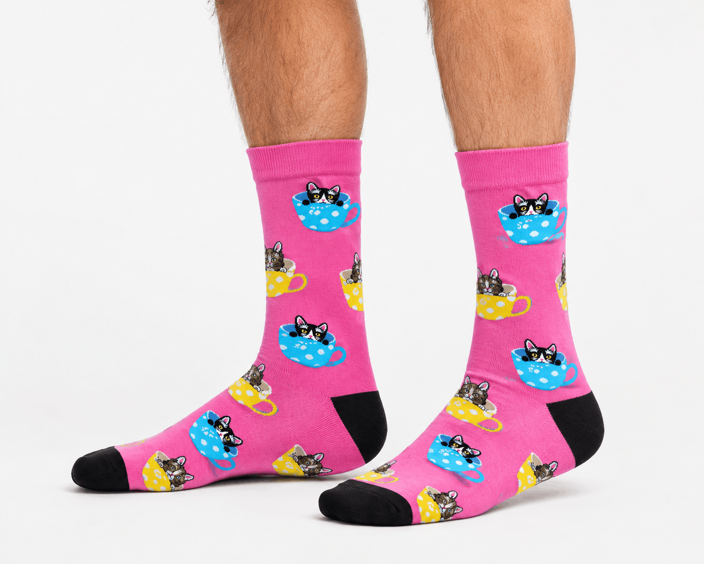 A pair of bright pink crew socks with a repeating pattern of cartoon cats lounging in teacups, worn on a person's feet against a clean white background.